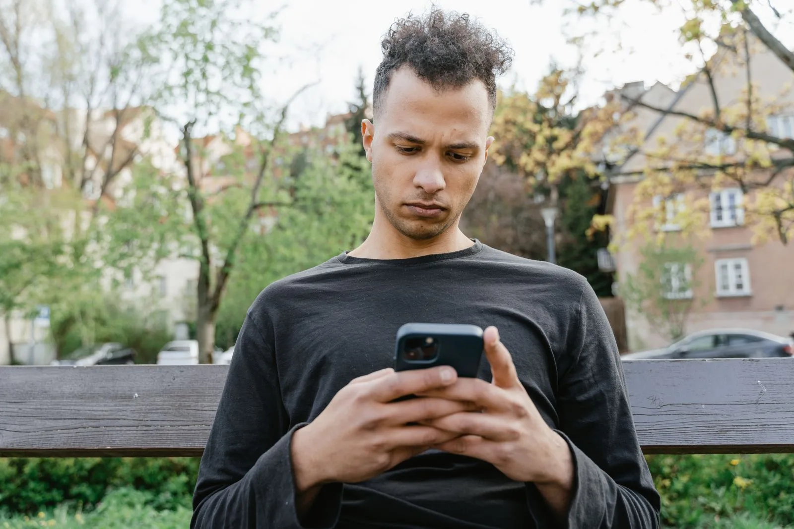 Dışarıda başı öne eğik şekilde telefonuna bakan genç adam